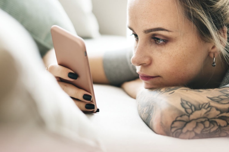 Besorgte Frau sucht mit dem Smartphone nach Hilfe bei einem Problem mit dem Tattoo
